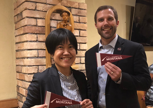 Miho Itabashi, left, and President Seth Bodnar hold small UM flags and pose for a photo